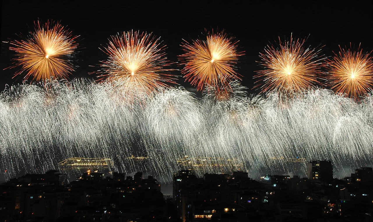 Queima de fogos do Réveillon na praia de Copacabana, no Rio de Janeiro, com o céu iluminado sobre a multidão de roupa branca na virada do ano
