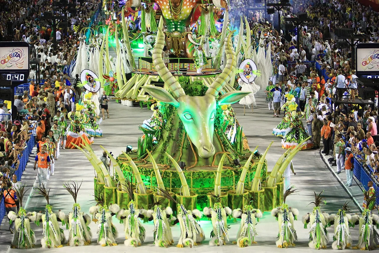 Desfile de escola de samba na Avenida Marquês de Sapucaí, no Sambódromo do Rio de Janeiro, com carro alegórico iluminado e arquibancadas lotadas de público à noite