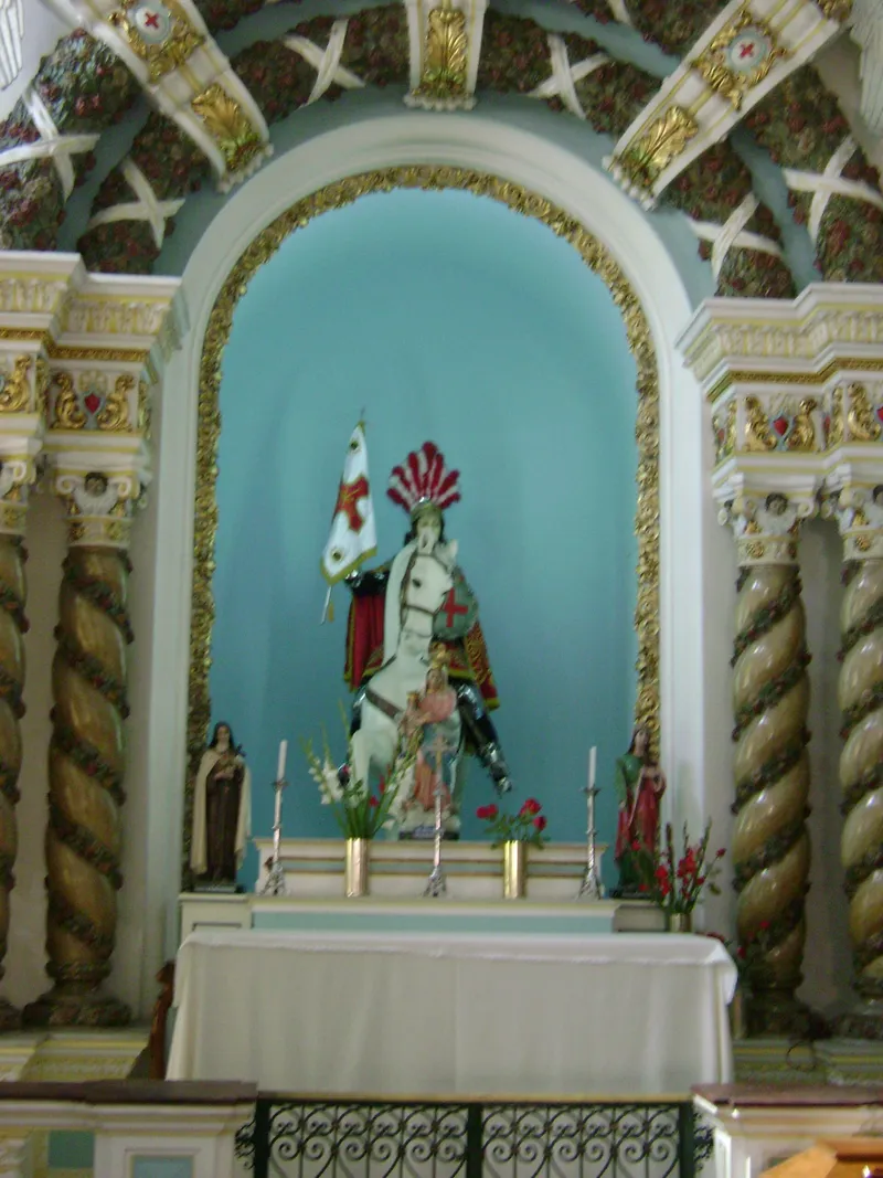 Imagem de São Jorge a cavalo, com capa vermelha e bandeira, num nicho azul de altar com colunas torcidas
