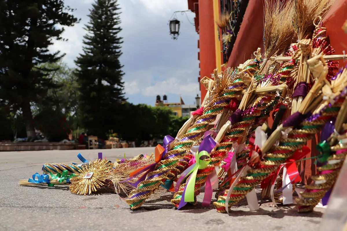 Cruzes e enfeites de palha trançada, com fitas coloridas, apoiados no chão do átrio de uma igreja