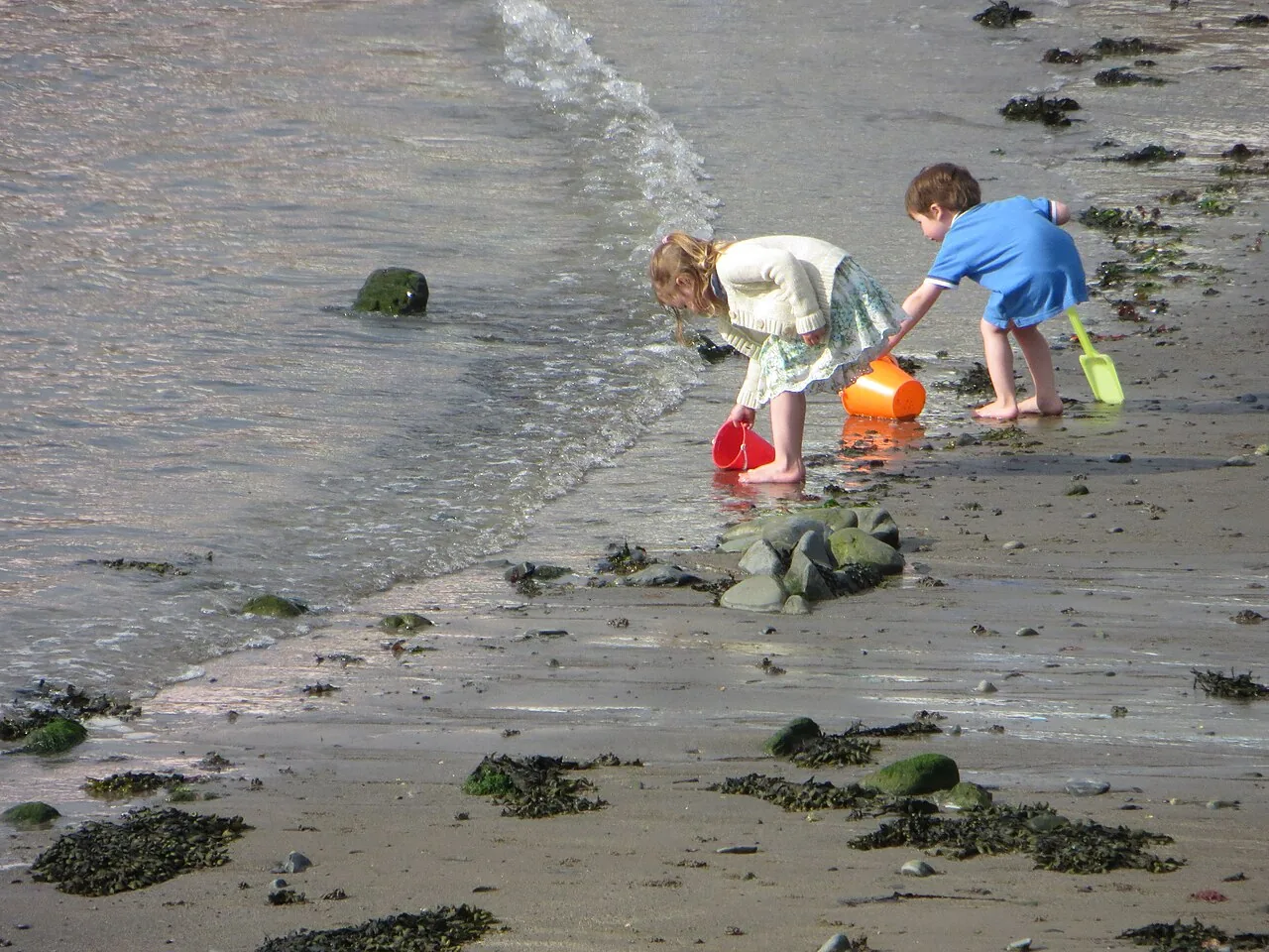 Duas crianças brincando com baldinhos e pás na beira da praia durante as férias escolares