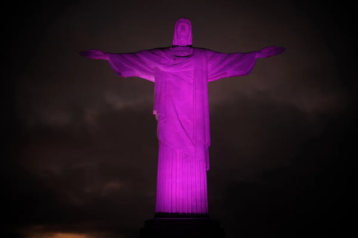 Estátua do Cristo Redentor iluminada de rosa contra o céu escuro da noite