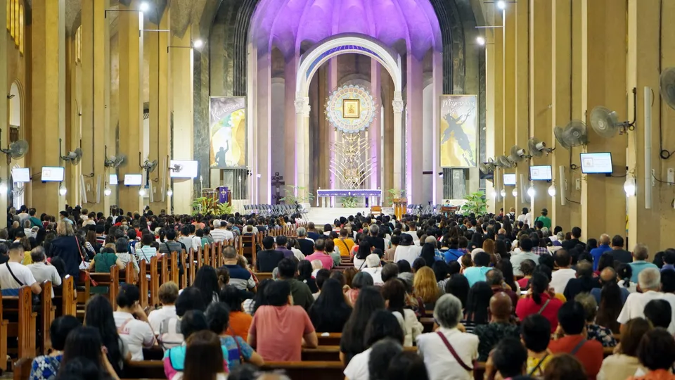 Igreja cheia de fiéis sentados nos bancos durante a missa, com o altar iluminado ao fundo