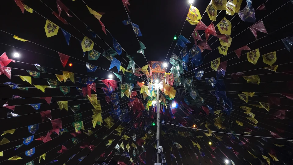 Bandeirinhas coloridas de festa junina penduradas em varais cruzados sob o céu da noite