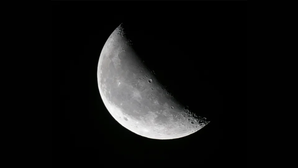 Lua minguante em forma de foice larga, iluminada de um lado, contra o céu negro