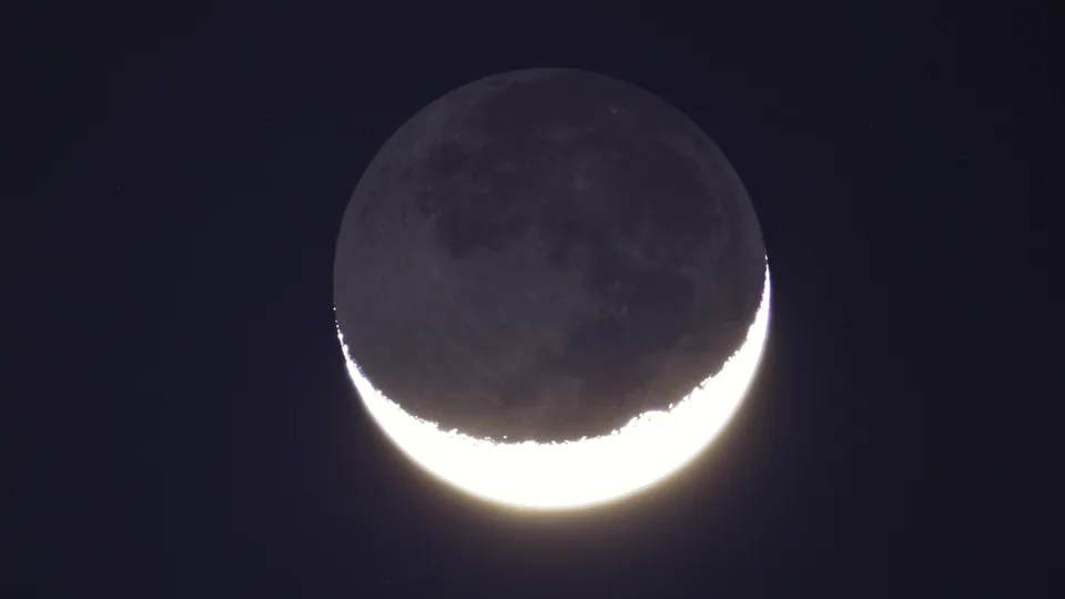 Lua com um filete fino e brilhante de luz na borda e o resto do disco fracamente visível, como fica poucos dias depois da Lua nova