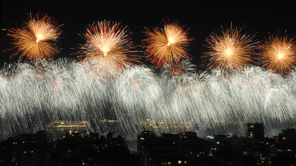 Fogos de artifício dourados e prateados sobre a praia de Copacabana na virada do ano, com navios e prédios iluminados